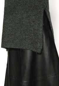 Pull gris en maille avec une texture côtelée, présentant des fentes latérales, associé à une jupe noire en cuir lisse, mettant en valeur leurs matériaux contrastés.