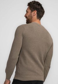 Beige knit sweater with ribbed texture, crew neck, and long sleeves. Features a fitted hem and subtle side details.