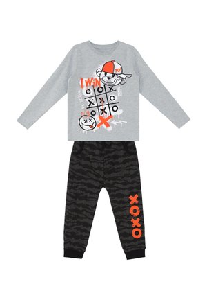 Langærmet grå top med kryds-og-bolle-design og tegneserie bjørn, kombineret med sorte mønstrede bukser med orange "XOXO" tekst på det ene ben.