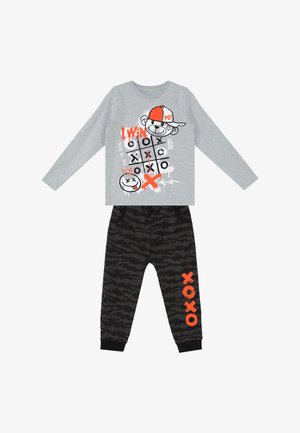 Langærmet grå top med kryds-og-bolle-design og tegneserie bjørn, kombineret med sorte mønstrede bukser med orange "XOXO" tekst på det ene ben.