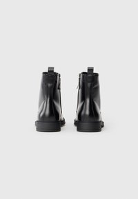 Botas de tobillo de cuero negro con un acabado suave, que cuentan con un cierre lateral con cremallera y una lengüeta, punta cuadrada y suela de goma resistente.