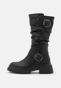 Czarne skórzane botki do połowy łydki z grubą podeszwą, luźnym cholewką i dwoma szerokimi paskami z kwadratowymi metalowymi klamrami.