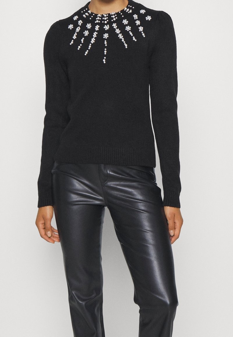 Pull noir orné de perles et de perles qui rayonnent à partir de l'encolure, associé à un pantalon en cuir noir.