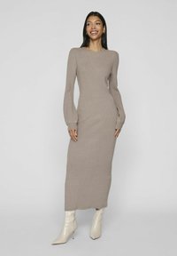 Abito a costine beige con maniche lunghe, silhouette aderente, scollatura rotonda e dettagli sottili sulle cuciture laterali, abbinato a stivali bianchi con tacco a spillo.