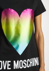Czarny t-shirt z dużym, gradientowym sercem w odcieniach różu, zieleni i niebieskiego, z napisem "LOVE MOSCHINO" grubymi, białymi literami na dole.