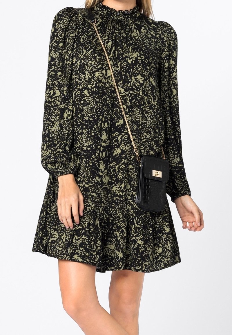 Vestido negro de manga larga con patrón floral verde, escote fruncido y falda acampanada. Combinado con un pequeño bolso negro con textura de cocodrilo.