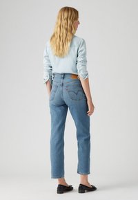 Ljusblå denimjeans med hög midja, raka ben och bakfickor. Modellen bär en ljusblå skjorta och svarta ballerinas.