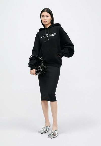 Černá mikina Off-White s logem, spárovaná s upnutou černou midi sukni. Obsahuje lesklou černou kabelku a metalické lodičky s špičatou špičkou.