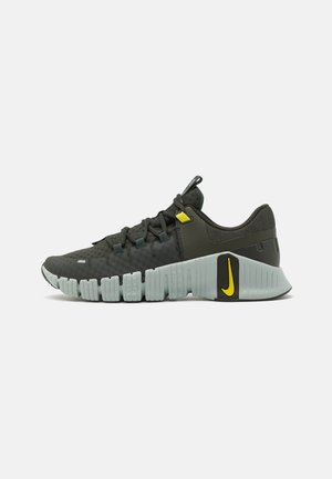 Chaussure de sport Nike noire et grise avec semelle segmentée, boucle de lacet jaune et virgule jaune Nike sur le côté du talon.