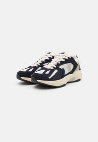 Scarpe sportive blu navy e crema con tomaia in rete traspirante, accenti testurizzati e suola ammortizzata. Presentano un design con lacci.