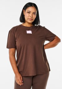 Brun bomull t-shirt med korta ärmar, med en rosa "I CAN CLUB" grafik på framsidan. Avslappnad passform och mjuk textur.
