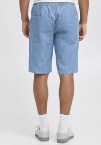 Shorts in denim azzurro chiaro, con cintura elastica e due grandi tasche posteriori. Tessuto liscio, lunghezza fino al ginocchio.