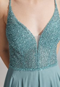 Teal mekko, jossa on paljetein päällystetty vartalo-osa, syvä pääntie, ohuet hihnat ja virtaava hame vaaleampaa teal-materiaalia.