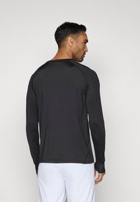 Juodas ilgos rankovės sportinis marškinėlis su apvaliu iškirpimu ir raglan stiliumi. Ypatinasi lygiu paviršiumi, siauru siluetu ir minimaliais siuvimo akcentais.