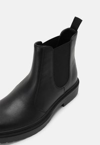 Bottes basses en cuir noir avec panneaux latéraux élastiques, bout arrondi et semelle en caoutchouc texturée pour une bonne adhérence et un confort optimal.