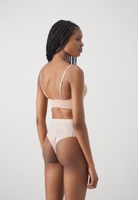 Naakt beha en hooggesneden slipset van zachte stof, met verstelbare bandjes, naadloze constructie en minimalistisch ontwerp.