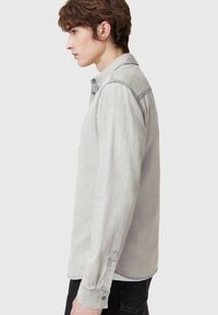 Helles graues Denimhemd mit geknöpftem Kragen, langen Ärmeln und Manschettendetails. Bietet eine lockere Passform und ein minimalistisches Design.