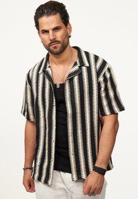 Das kurzärmelige Hemd zeichnet sich durch schwarz-creamfarbene Streifen mit einem geometrischen Muster aus. Es besteht aus strukturiertem Stoff und verfügt über einen Kragen sowie eine Knopfleiste.