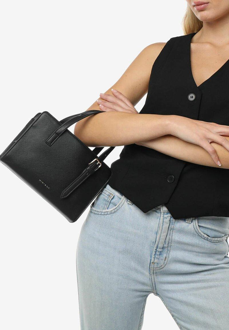 Sort, tekstureret mini handbag med struktureret form, korte håndtag og spændeakcent. Båret over en sort top og lyseblå jeans.