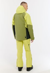 Skijacke und -hosen in leuchtendem Gelb und Grün. Die Jacke hat eine Kapuze, Farbblöcke und ein Logo-Tag. Die Hose hat Reißverschlusstaschen und Belüftungen.