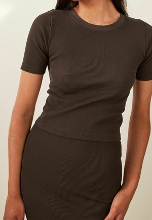 Woman wearing a fitted, short-sleeve, ribbed dark brown top and matching skirt, shown from neck to hips against a plain background.