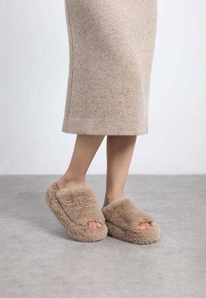 Zapatillas de casa beige difusas con un diseño de punta abierta y un material suave y texturizado. Forma redondeada con una apariencia lujosa y acogedora.