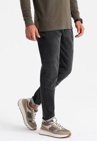 Černé džíny se zúženým střihem, zdobené záplatami, v kombinaci se světle zbarvenými sportovními botami s béžovými a šedými akcenty.