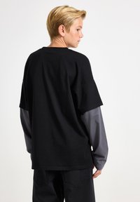 Schwarzes Baumwoll-T-Shirt mit lockerer Passform, kurzen Ärmeln und grauem Langarmuntershirt. Einfache Gestaltung, keine sichtbaren Muster oder Akzente.