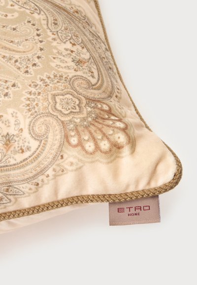 Coussin décoratif beige avec un motif cachemire complexe et une bordure tressée, présentant une étiquette visible portant la mention "ETRO HOME" sur fond blanc.