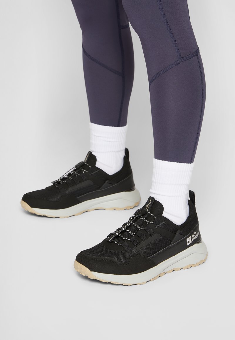 Sneaker sportivi neri con tomaia in mesh testurizzato, lacci bianchi e suola beige. Accoppiati con leggings scuri e calzini bianchi alla caviglia.