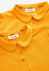 Dvé žluté polo trička mají límečkový design, texturovanou tkaninu a knoflíky ve tvaru srdce, s logem "Clarks" na krku.