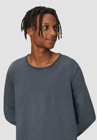 Chemise à manches longues bleu foncé avec un col large et un tissu texturé, présentant des coutures visibles le long des bords.