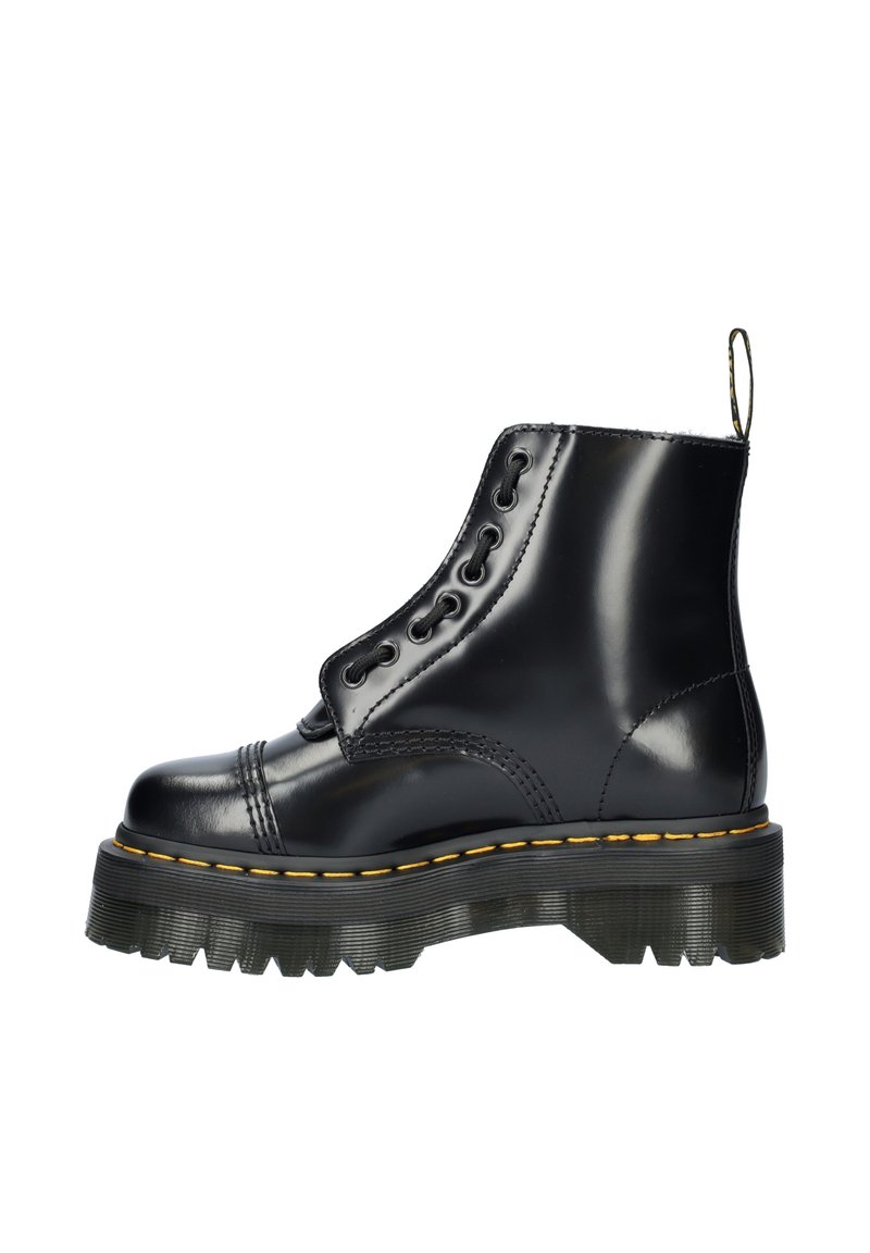 Bottine en cuir noir avec une semelle à crampons épaisse, présentant un laçage décoratif, un empiècement cousu jaune et une languette au niveau du talon.