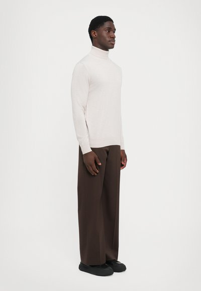 Maglione beige chiaro a collo alto in un morbido punto, abbinato a pantaloni palazzo marroni e sneakers nere. Design minimalista con polsini a coste.