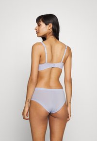 Set di lingerie viola chiaro con bordi scallop, spalline regolabili e una texture di tessuto liscia, che mostra un perizoma e un reggiseno di spalle.