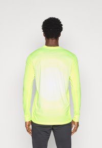 T-shirt de sport à manches longues en jaune néon vif, présentant un motif de dégradé circulaire subtil et un tissu lisse et léger.
