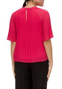 Blusa fucsia plisada con mangas cortas, detalle de abertura en la espalda y tejido ligero, combinada con pantalones negros.