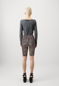 Grå långärmad tröja kombinerad med högmidjade shorts i leopardmönster. Klädseln inkluderar svarta platåskor.