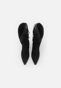 Botas de tobillo de ante negro con punteras en punta, flecos decorativos y acentos joya embellecidos en la parte superior y en las punteras.