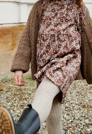 Robe fleurie marron associée à un cardigan en maille texturée, collants beige clair et bottines noires ; mise en valeur du motif floral et du jeu de superpositions.