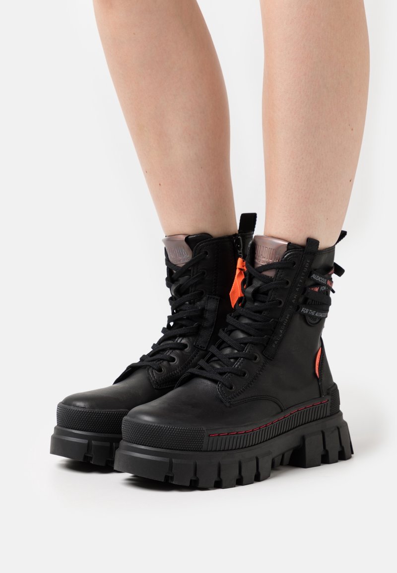 Stivali alla caviglia in pelle nera con suola in gomma spessa, design con lacci, dettagli arancioni e collare imbottito per un comfort maggiore.