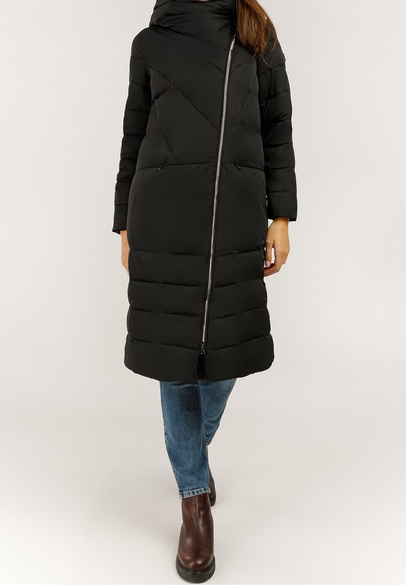 Abrigo puffer negro con cuello alto, patrón acolchado horizontal, cierre frontal, dos bolsillos laterales y mangas largas. Combinado con jeans y botas.