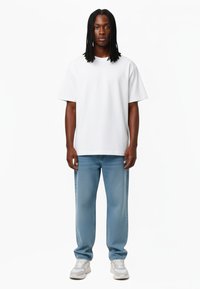 Bijela pamučna majica s kratkim rukavima, uparena sa svijetloplavim trapericama i bijelim tenisicama. Jednostavan, opušteni kroj i glatka textura.