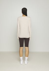 Light beige long-sleeve top with small speckles, paired with dark brown cycling shorts. The outfit is complemented by white socks and sneakers.