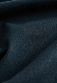 Țesătură de un albastru închis cu o textură moale și netedă, având un model de țesătură subtil. Prezintă pliuri aspre care surprind lumina și umbra.