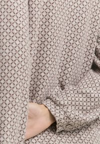 Hand gedeeltelijk in de zijzak van beige, gestructureerde kleding met een diamantpatroon gestoken.