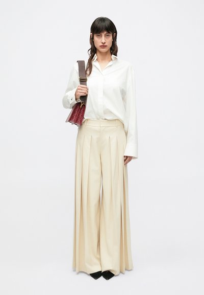 Biała koszula na guziki, kremowe plisowane spodnie o szerokich nogawkach oraz bordowa torebka o fakturowanym wykończeniu. Całość dopełniają czarne wysokie obcasy.