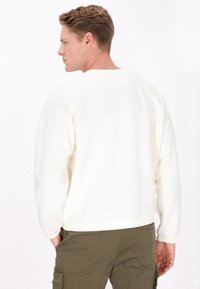 Sweatshirt blanc à col rond avec manches longues, texture douce et poignets côtelés, associé à un pantalon cargo olive. La vue arrière montre un design simple.