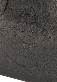 Črna usnjena torbica z vtisnjenim logotipom "JOOP! JEANS" v krožnem dizajnu, teksturirana površina s finimi vzorci.