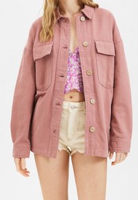 Różowa, oversize'owa kurtka wykonana z bawełny, z dwoma przednimi kieszeniami, zapięciem na guziki i luźnym krojem. Noszona na kwiecistym crop topie.